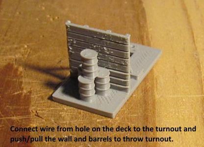 N Scale -- Deck for switch machine with a wood wall and 4 barrels in front of the wall.