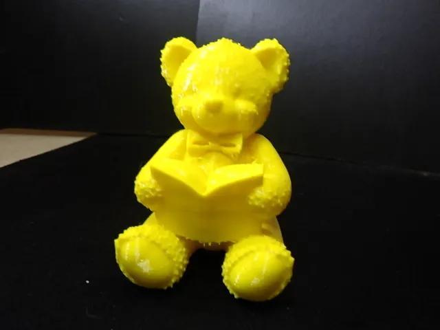 A cute teddy bear sitting down reading a book.   